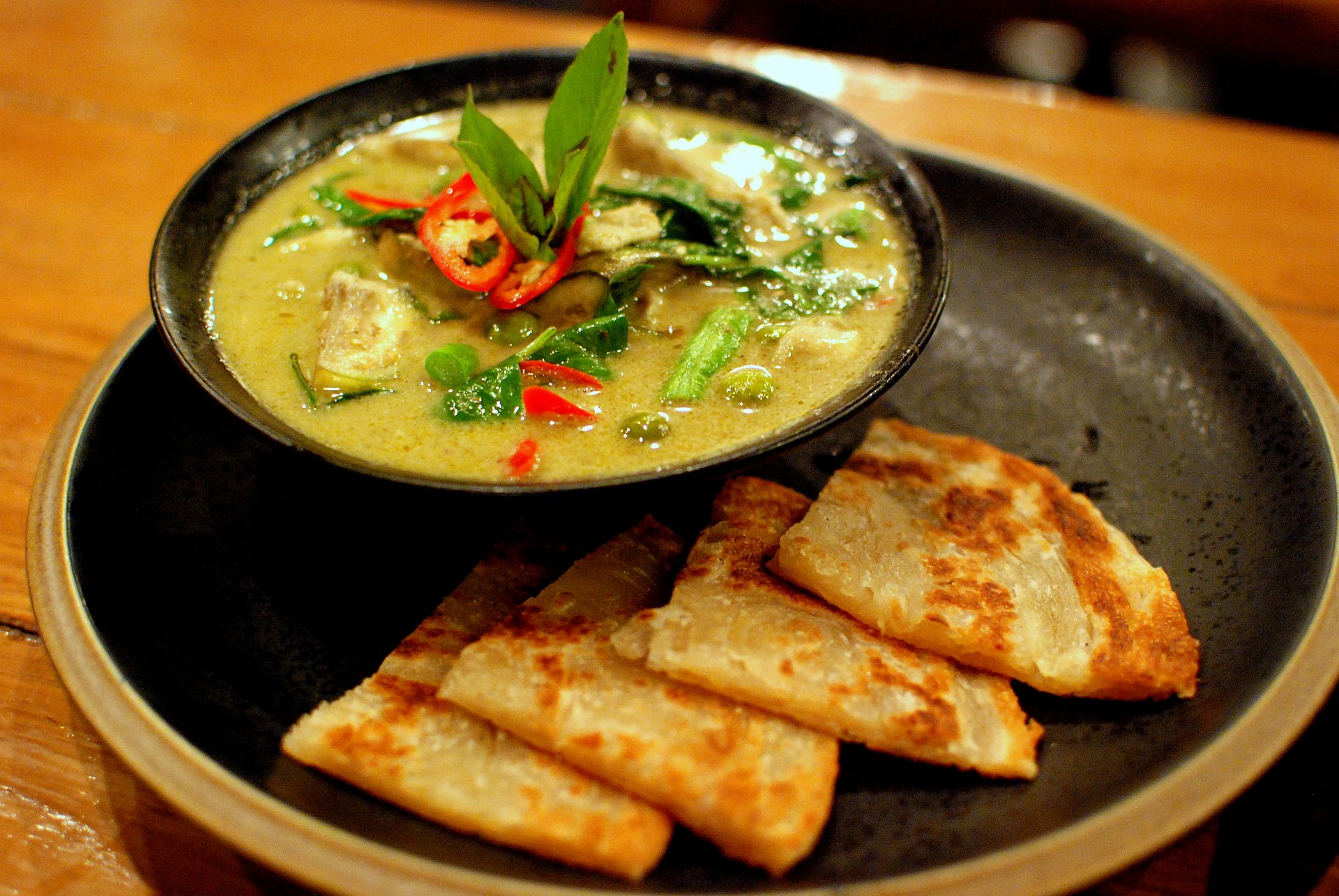 Thai green curry with chicken and Thai basil in a dark bowl, coconut sauce, jasmine rice beside, Natural window light, ivory linen, handmade ceramic, shallow depth of field, no text, no logo, no watermark, fine-dining magazine photograph. Green Curry Chicken