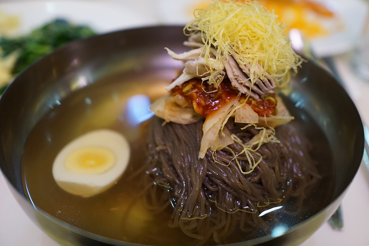 Photoreal photograph of the finished dish Pyongyang cold noodles (랭면), the actual plate from North Korea, handmade ceramic, natural window light, shallow depth of field, no text, no logo, no people, Natural window light, ivory linen, handmade ceramic, shallow depth of field, no text, no logo, no watermark, fine-dining magazine photograph. Pyongyang cold noodles