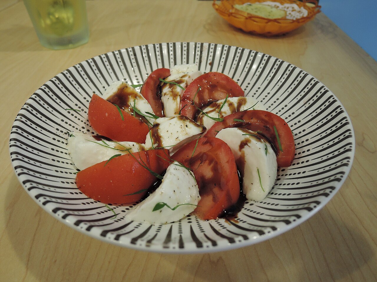 Sliced tomato and mozzarella with basil and olive oil on a white plate, Natural window light, ivory linen, handmade ceramic, shallow depth of field, no text, no logo, no watermark, fine-dining magazine photograph. Tomato and Mozzarella